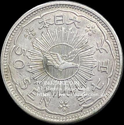 八咫烏銀貨は初めて一般公募による図案が採用されました。  表中央の価額の左右に鳳凰、裏面日章の真ん中に八咫烏が配されています。  銀価格高騰の為、流通しませんでした。  八咫烏50銭銀貨は直径24.85mm 品位は銀800 / 銅200 量目は6.75gです。  大正7年（1918）鑑定書付。